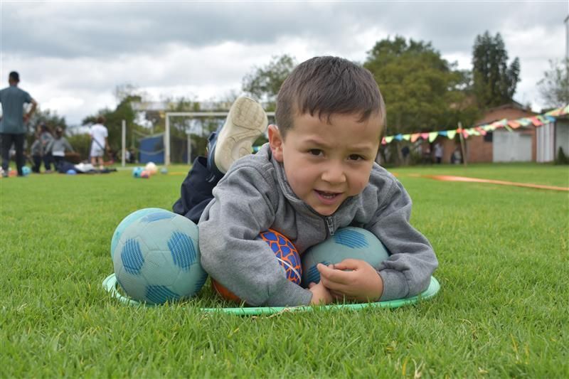 Un niño tumbado en el césped con balones de fútbol azules, sonriendo en un parque.