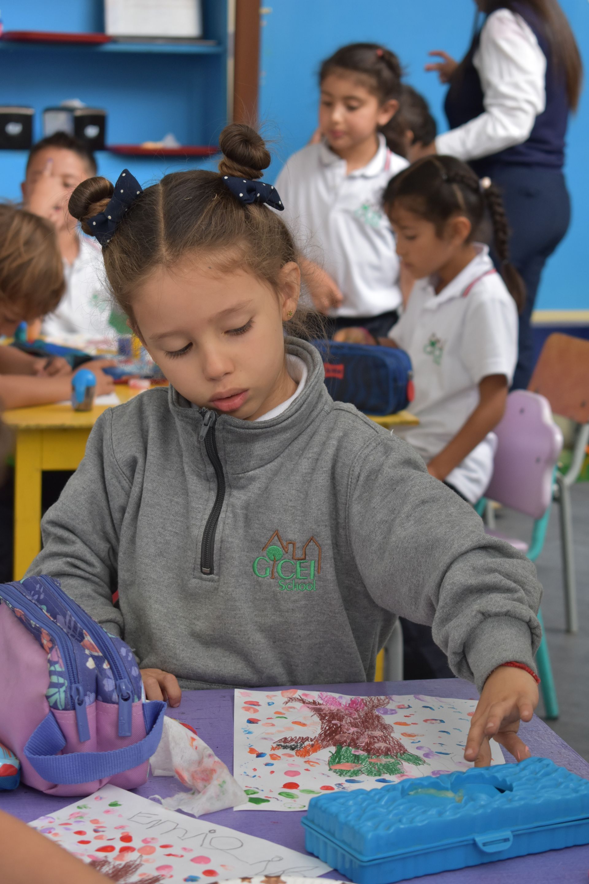 Un niño dibuja en un pupitre mientras otros alumnos trabajan al fondo.