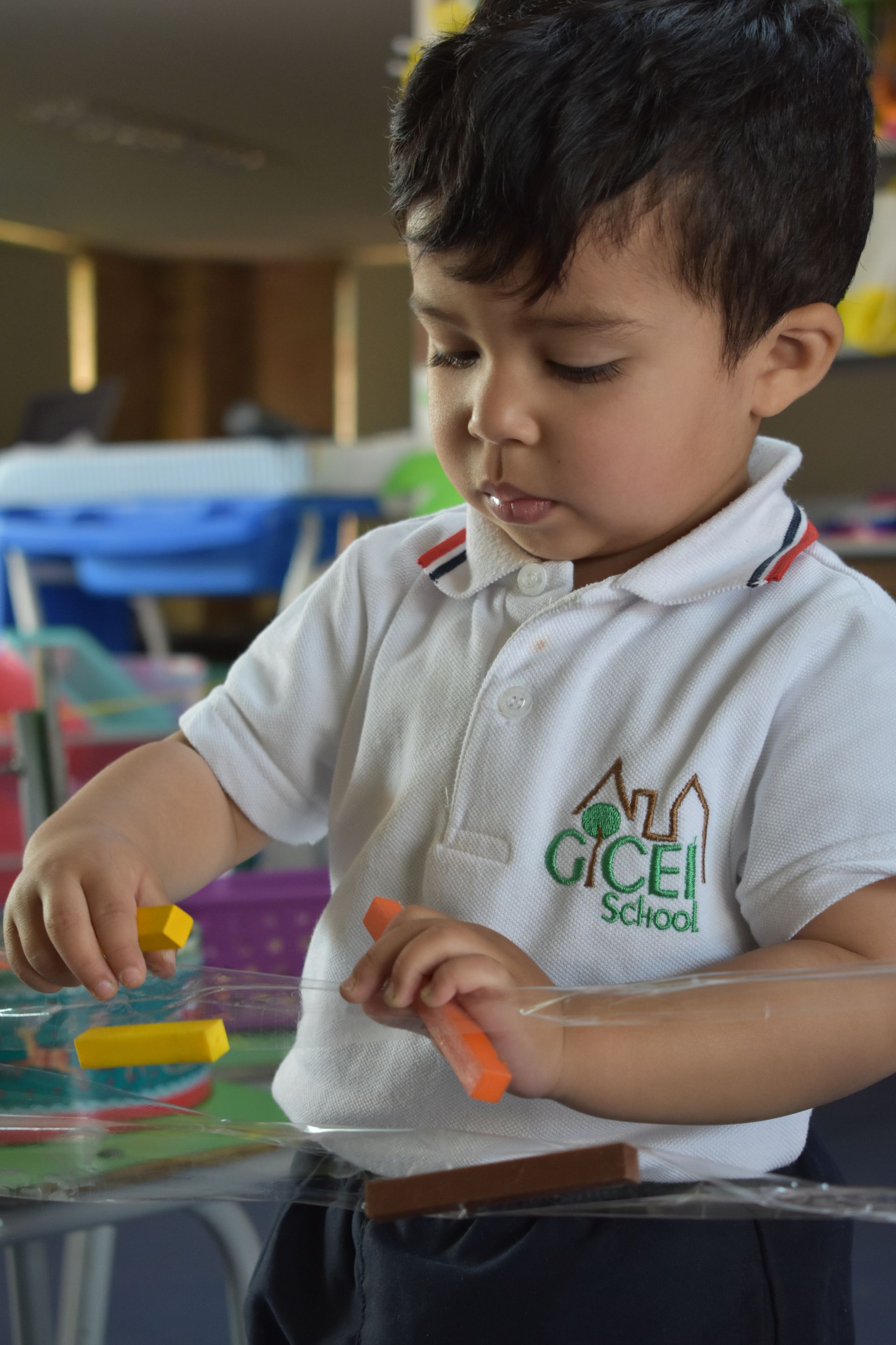 Un niño con un polo escolar blanco apila anillos de colores en una mesa en un aula.