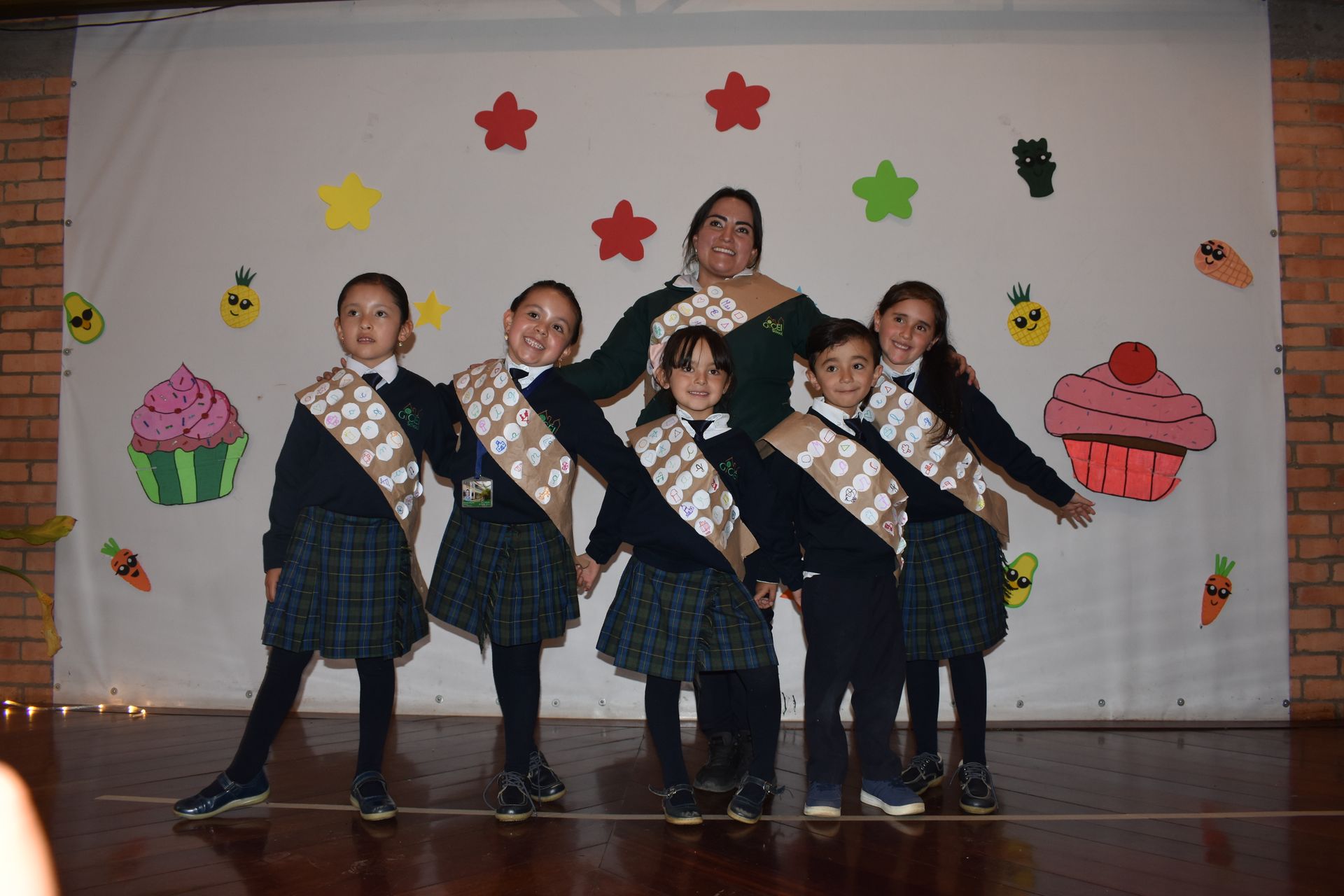 Cinco niños y una maestra posan en un escenario decorado durante una función escolar.