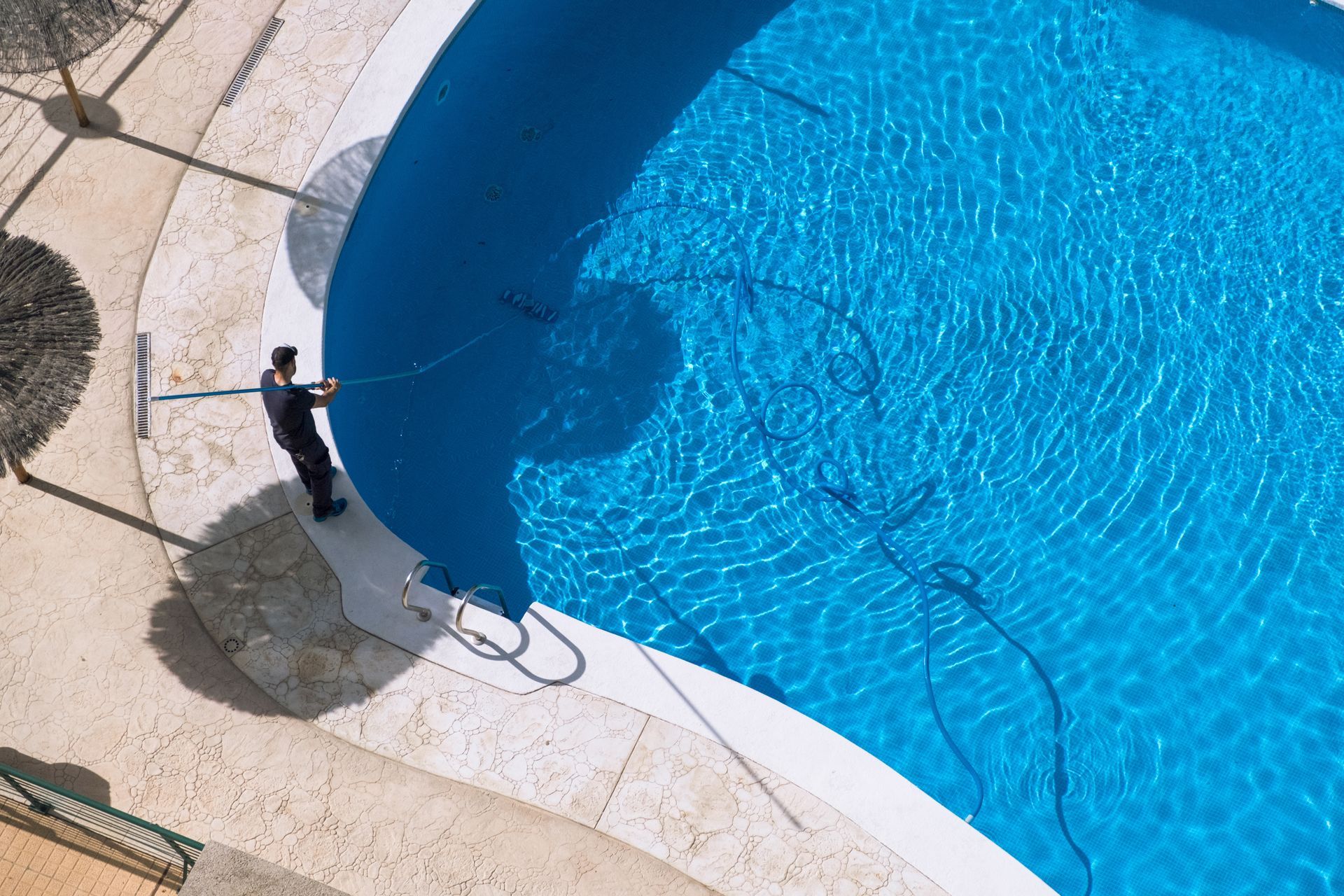 A man is cleaning a swimming pool with a broom.