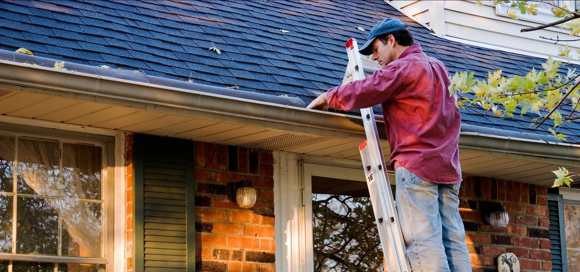 A man is standing on a ladder working on the roof of a house.