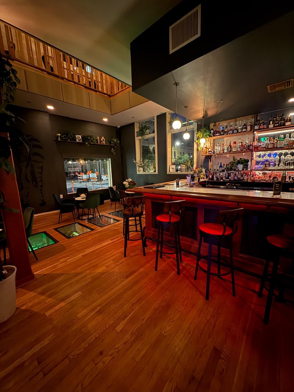 Interior view of a dimly lit bar with a wooden floor, bar stools, and a well-stocked bar.