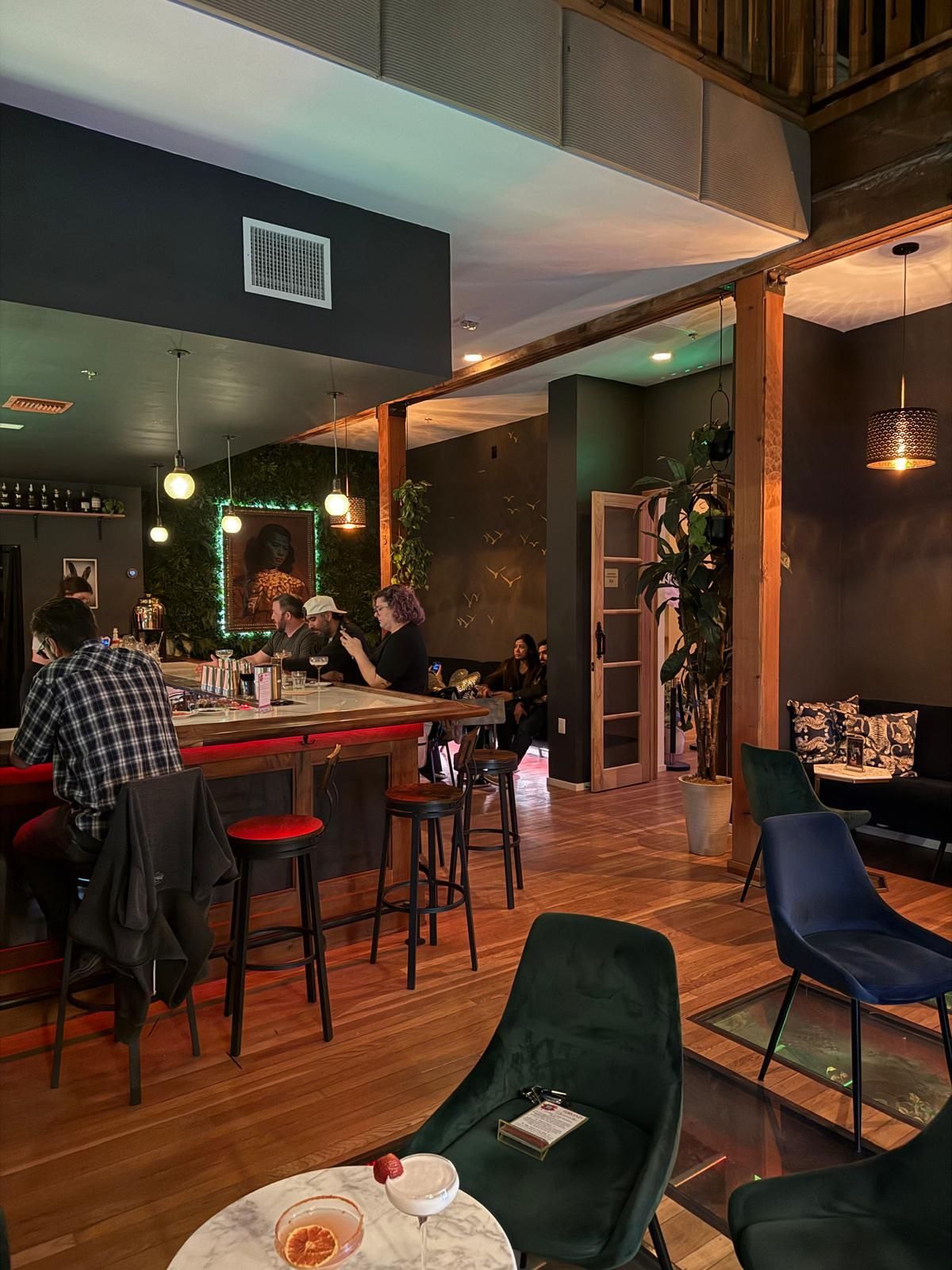Interior of a bar with people seated at a red bar and at tables with dark blue and green chairs.