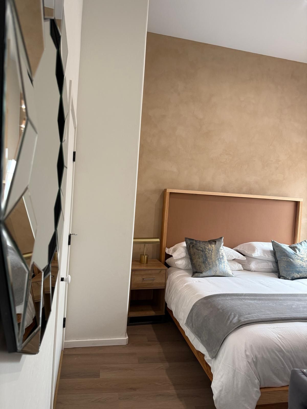 Bedroom with bed, nightstand, textured wall, and angled decorative mirror.
