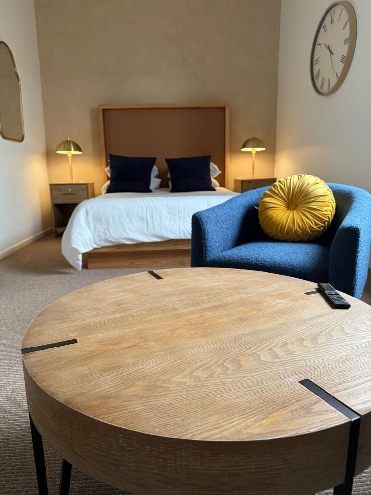Bedroom with a bed, blue armchair, round wooden coffee table, and a wall clock.