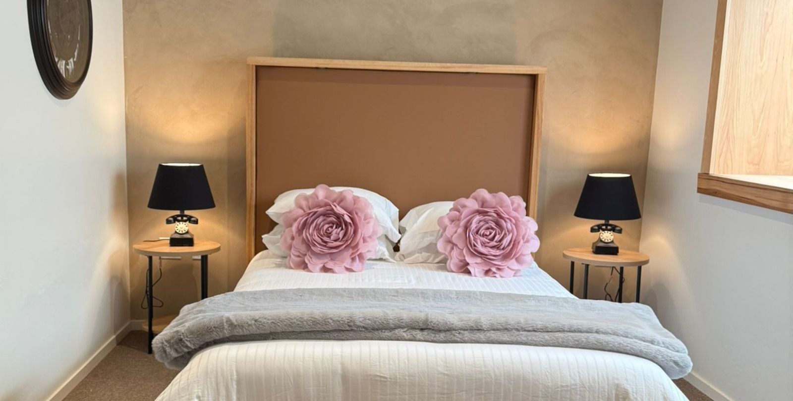 Bedroom with bed, pink floral pillows, black lamps on side tables, and brown headboard.