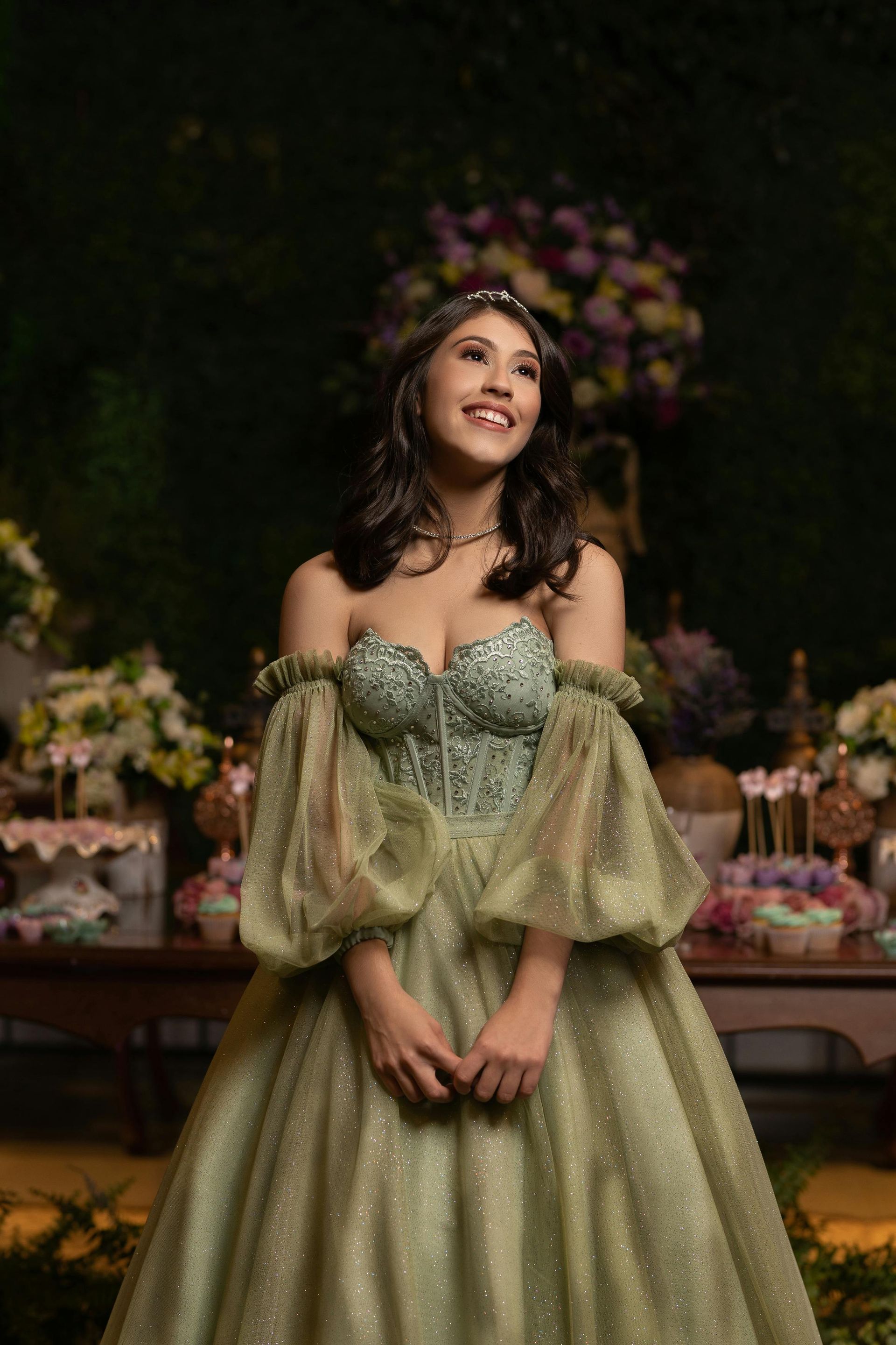 Woman in a green ballgown, smiling, with decorations in background.