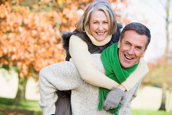 Smiling couple in autumn park, woman riding on man's back; green scarf and warm sweaters