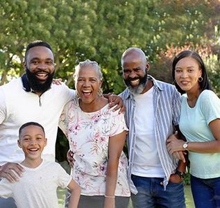 Family of five smiling outdoors in a park, with trees in the background.