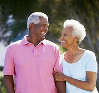 Smiling couple walking outdoors, the man in a pink polo shirt and the woman in a white top.