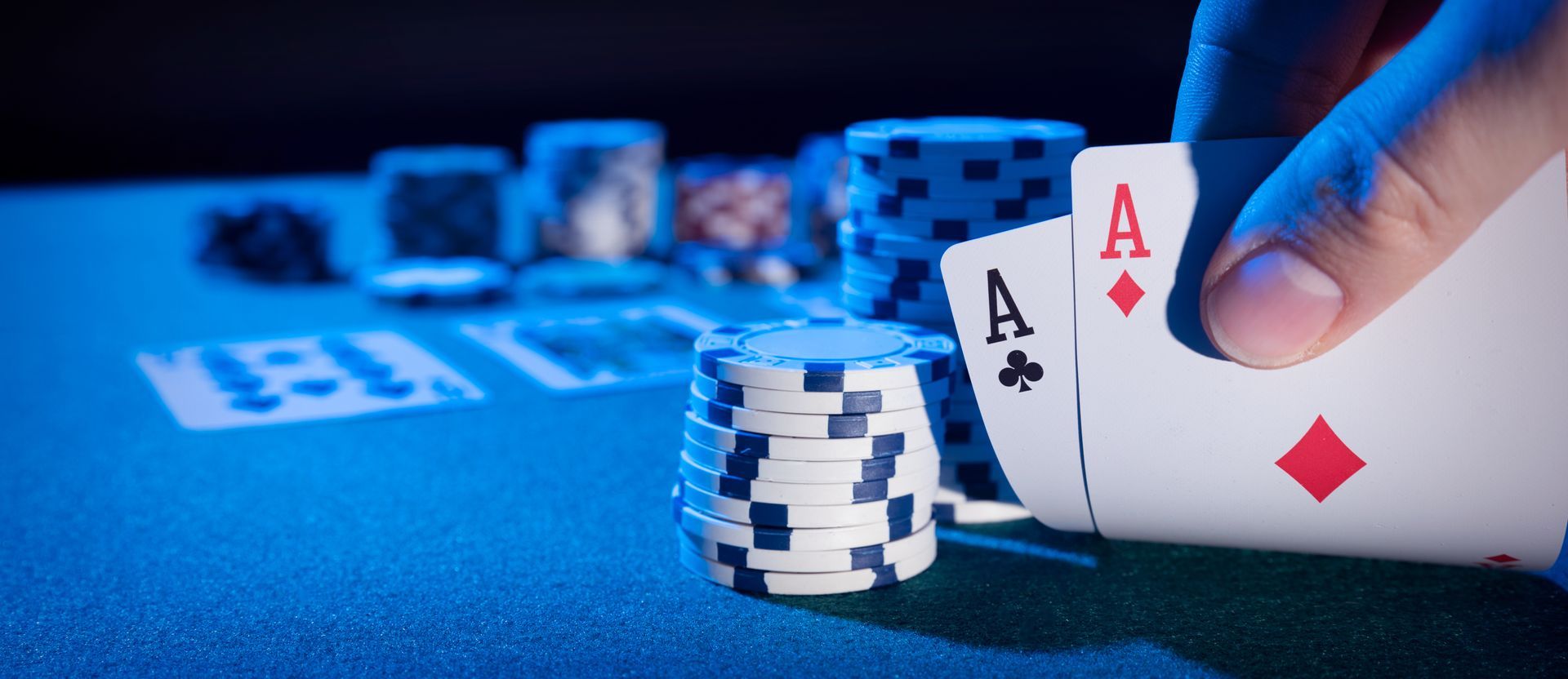 Hand holding two Aces over a poker table with chips and cards.