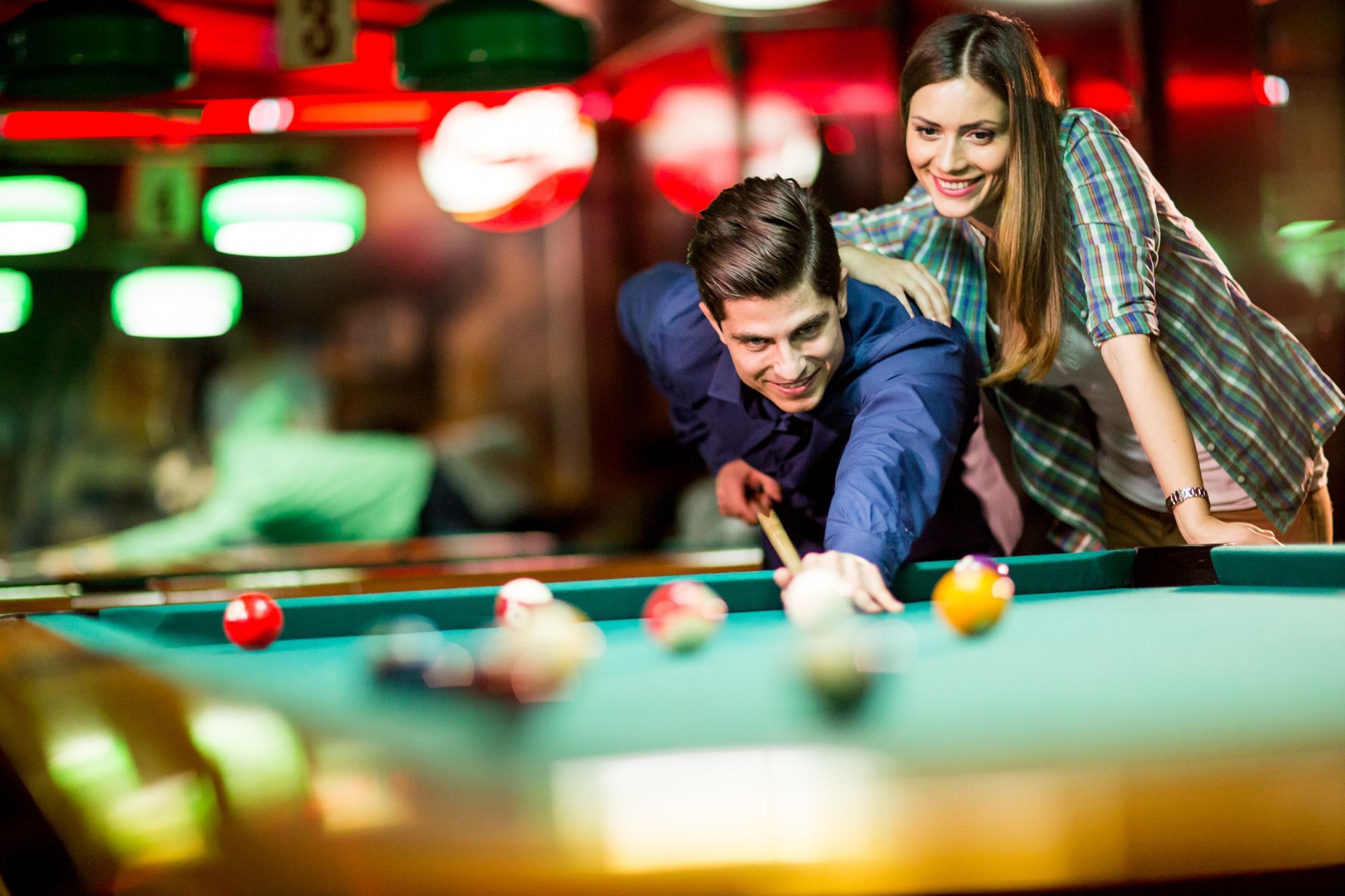 Man playing pool with a woman smiling and watching in a dimly lit bar.