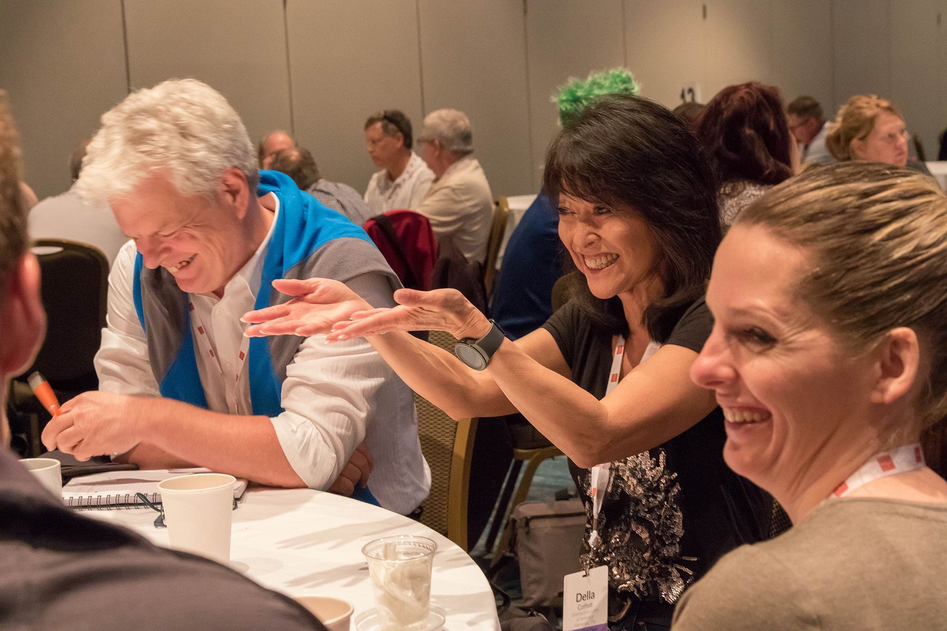 People at a table, smiling and gesturing in a meeting setting.