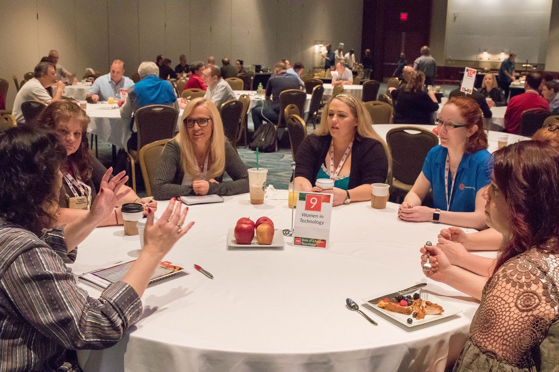 People seated at round tables in a conference hall, engaging in conversation and collaboration.