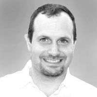Man with dark hair smiling at the camera, wearing a white shirt; black and white portrait.