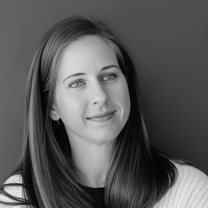 Woman with long, straight hair, smiling, looking away from the camera. Black and white, against a solid background.