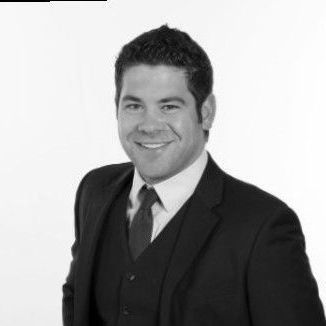 Man in a suit, smiling. Wearing a tie, vest, and button-up shirt. Black and white photo.