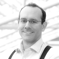 Man wearing glasses and suspenders, smiling. Black and white photo.