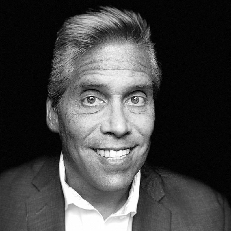 Smiling person in a suit jacket, against a dark background.