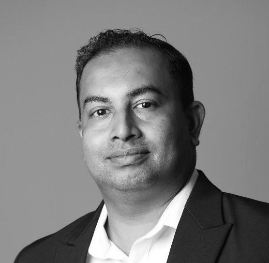 Man in a blazer and open-collared shirt, looking at the camera. Black and white photo.