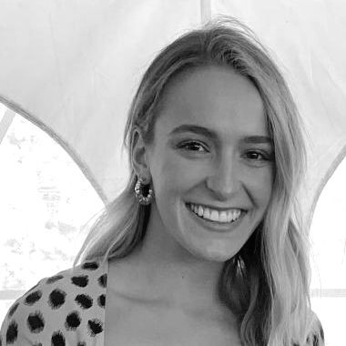 Woman with blonde hair smiles, wearing hoop earrings and a spotted top.