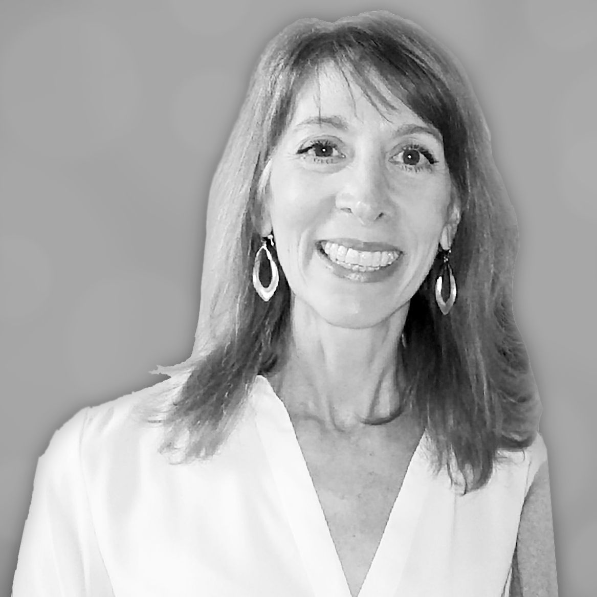 Woman smiling, wearing a white top and hoop earrings, against a gray background.