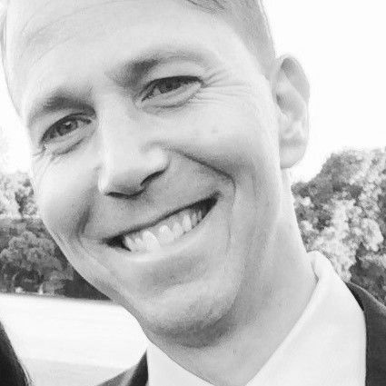 Man smiling, looking towards the camera, wearing a collared shirt. Black and white photo.