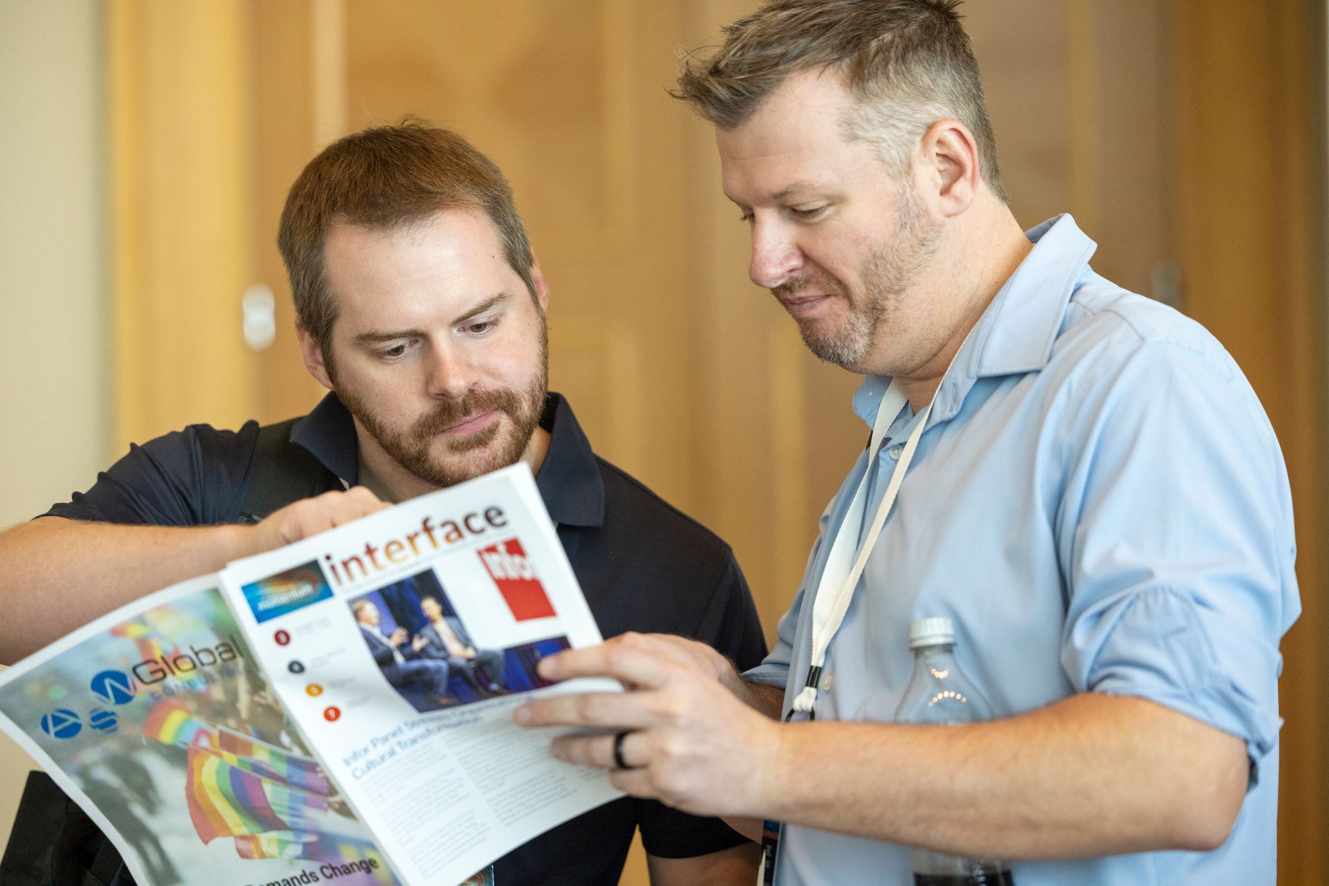 Two men looking at a magazine called "Interface" with colorful cover, in a light-filled setting.