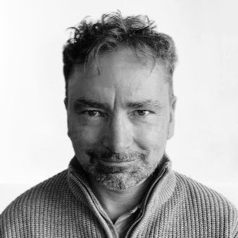 Man with curly hair and a beard, wearing a textured sweater, looking at the camera.