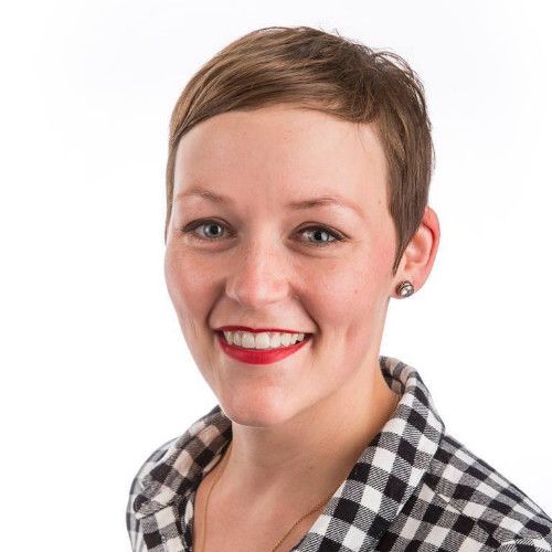 A woman with short hair is smiling and wearing a plaid shirt.