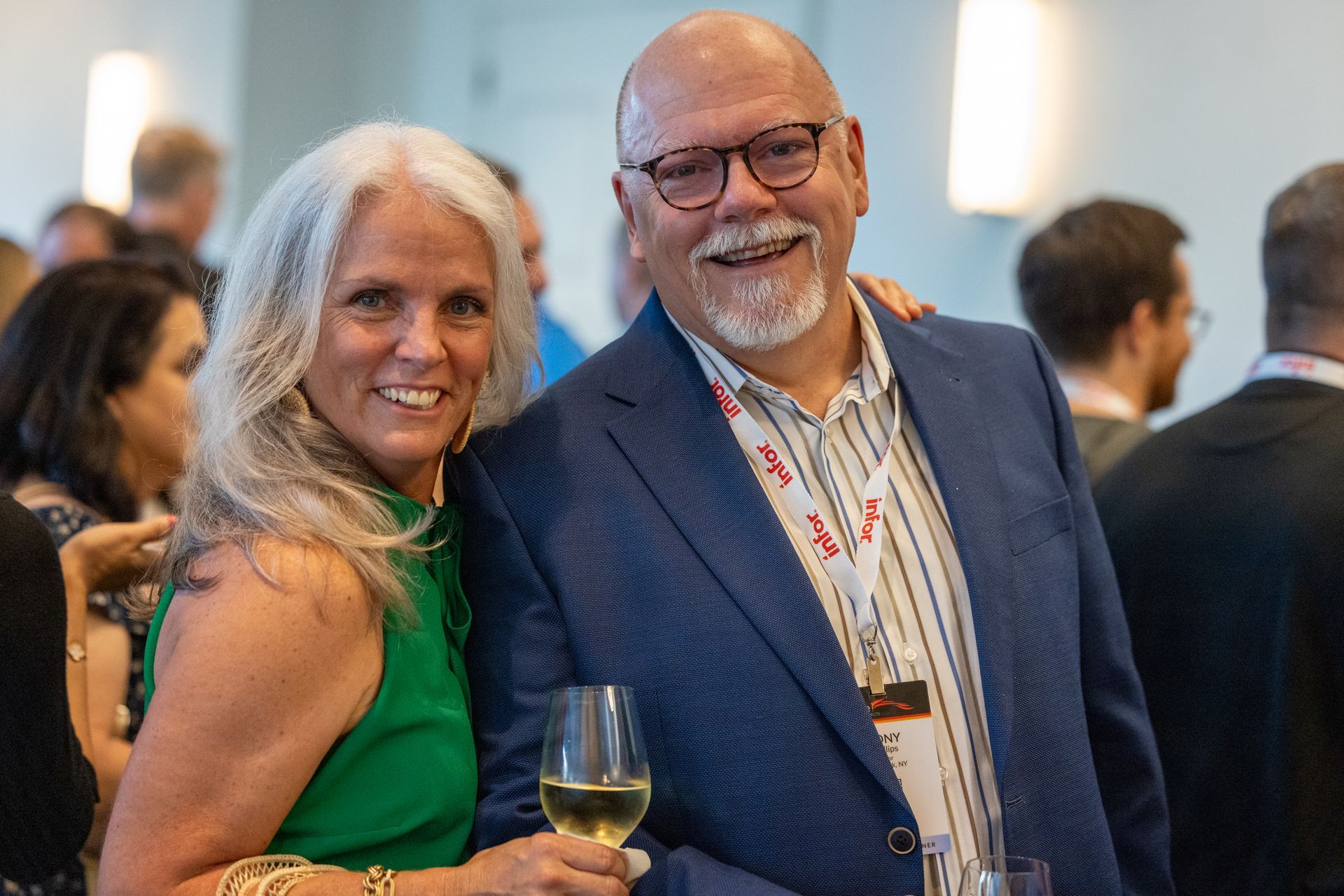 Woman in green dress and man in blue blazer smile, holding drinks at event.