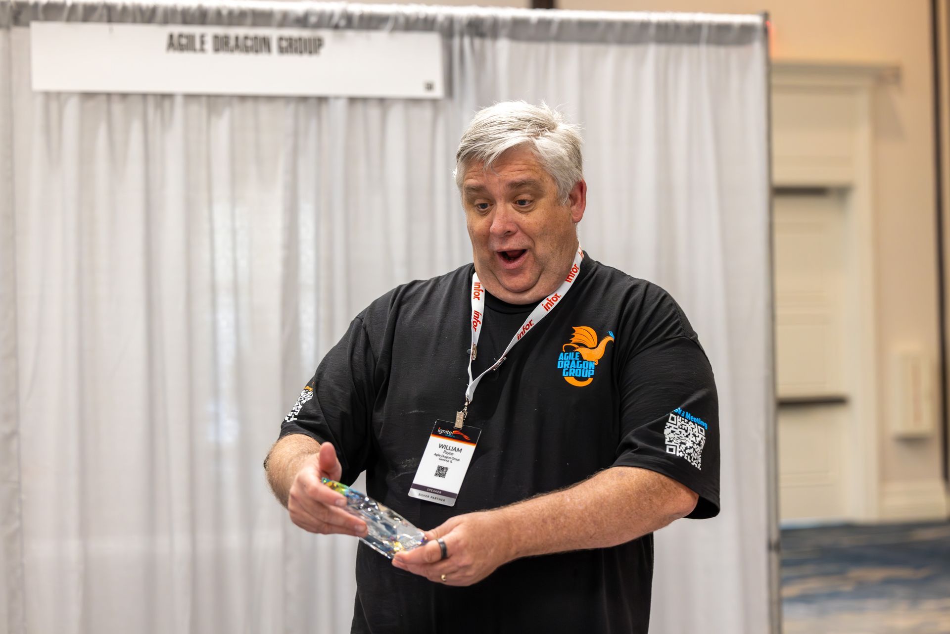 Man with surprised expression holding an object at a trade show booth labeled 