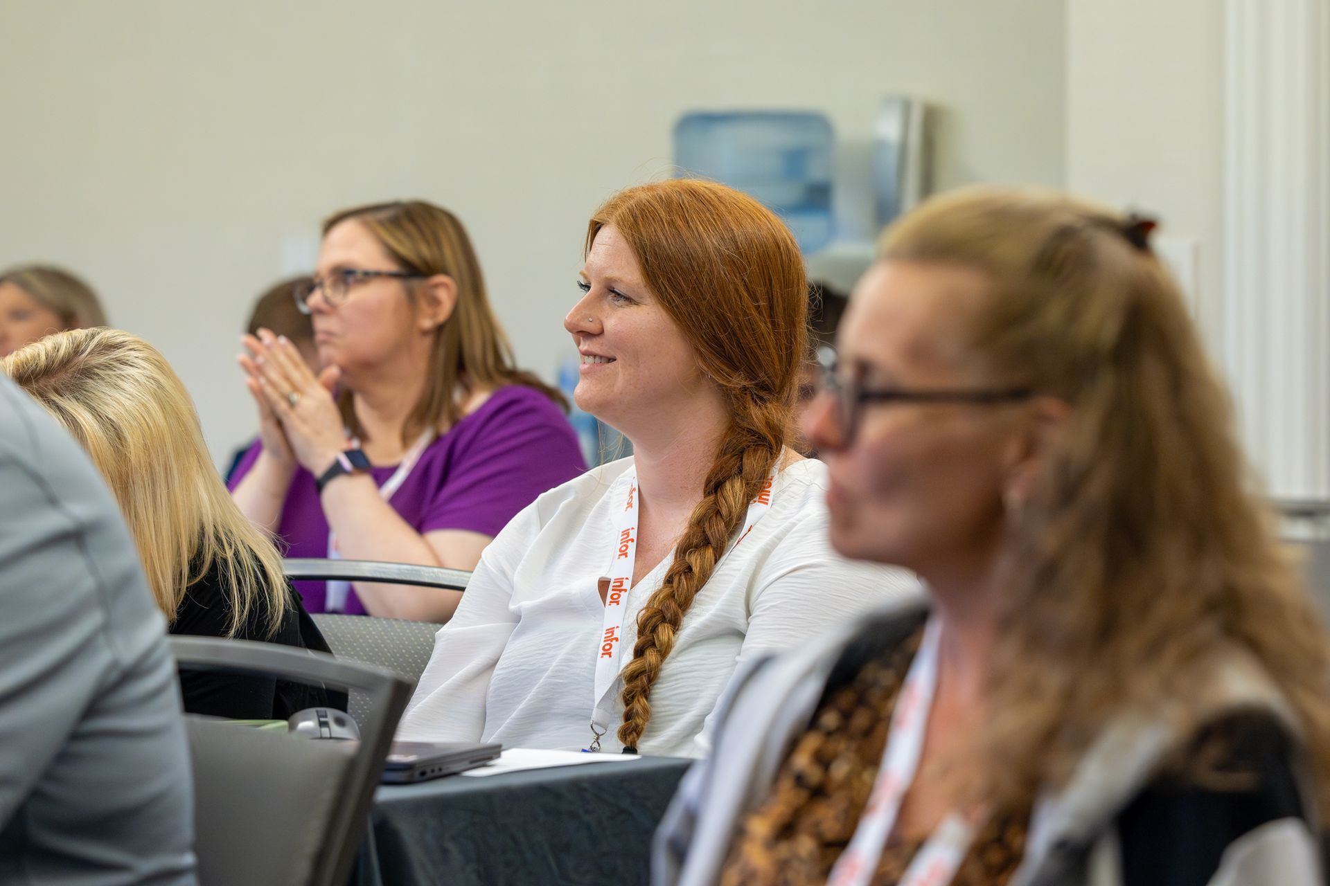 People in a conference setting. Woman with long red braid smiles, others listen and clap.