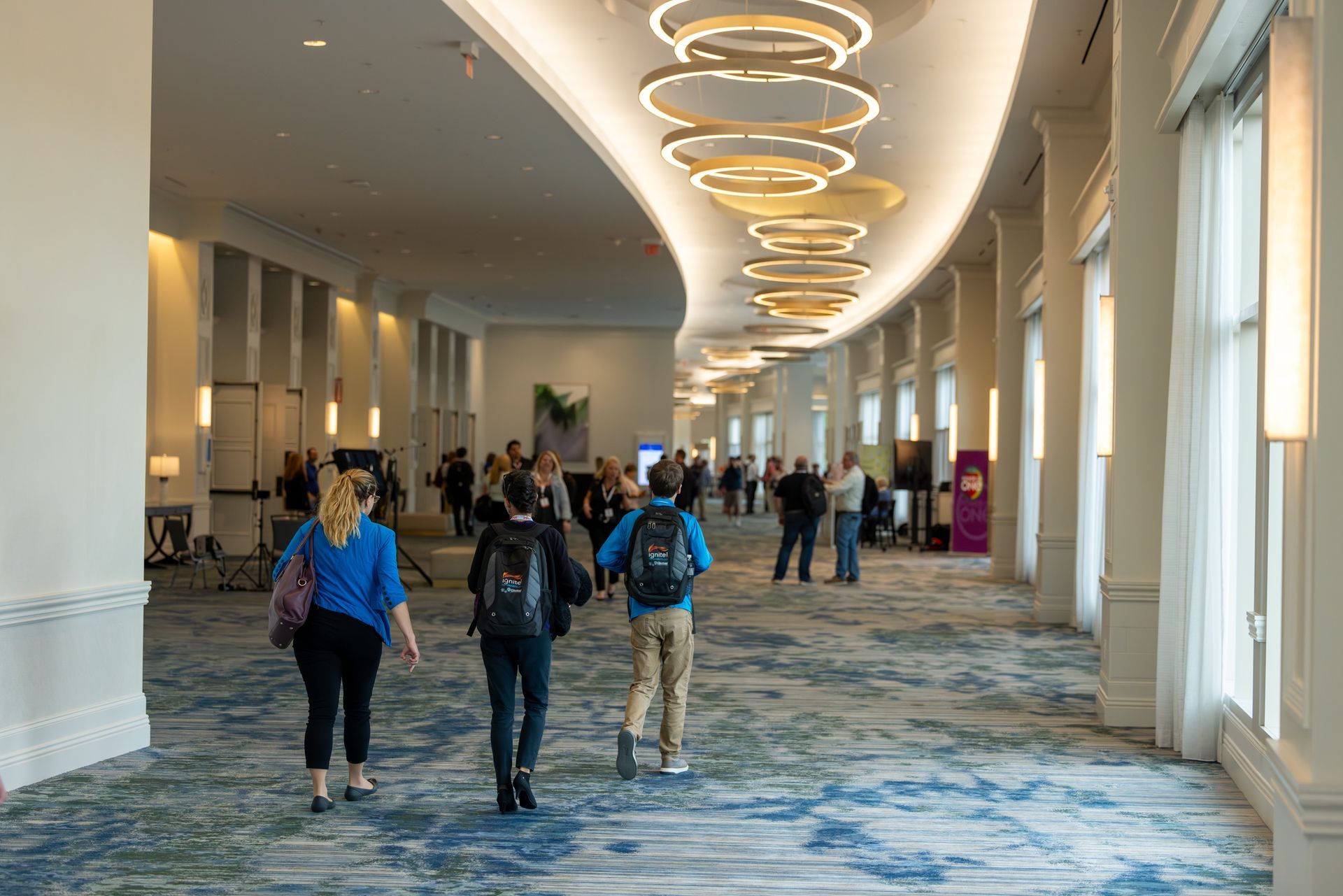 Hallway with people walking; ornate ceiling lights and patterned carpet.