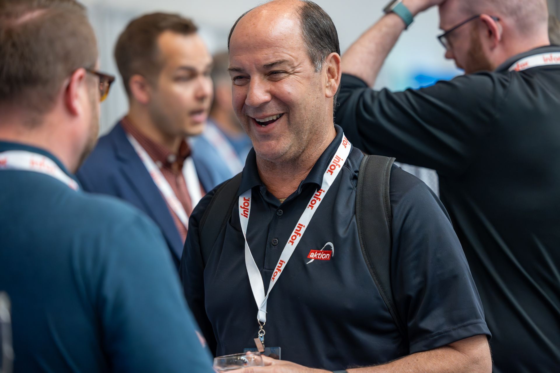 Man smiling and talking with other people, wearing black shirt and lanyard at an event.