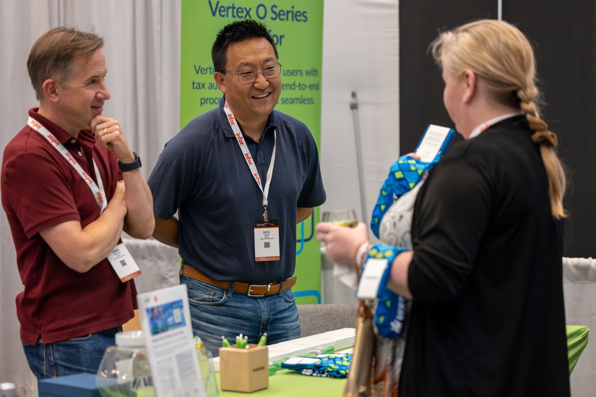 Three people talking at a trade show booth; two men and a woman. The man in the middle is smiling.