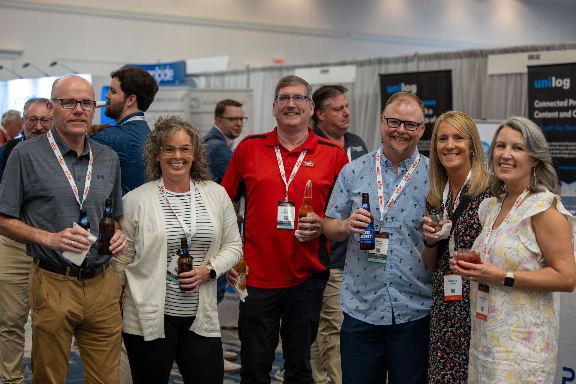 Group of people at an event, holding drinks, smiling. Some have lanyards.