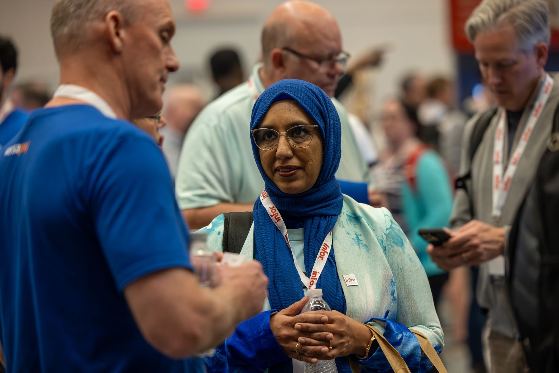 Woman in hijab talking to a man in blue shirt at an event. Other people are in the background.