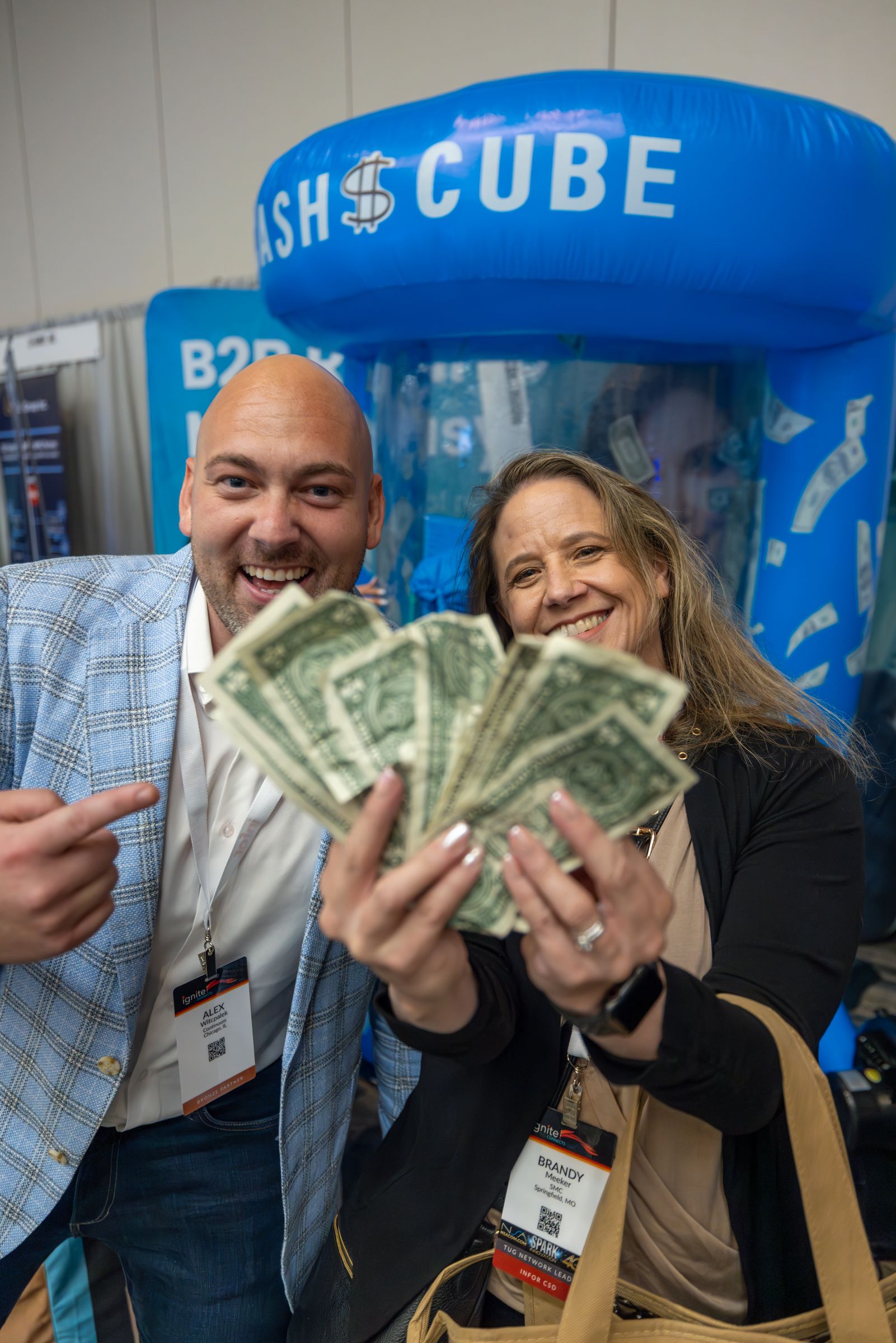 Man and woman smiling, holding cash, near a 