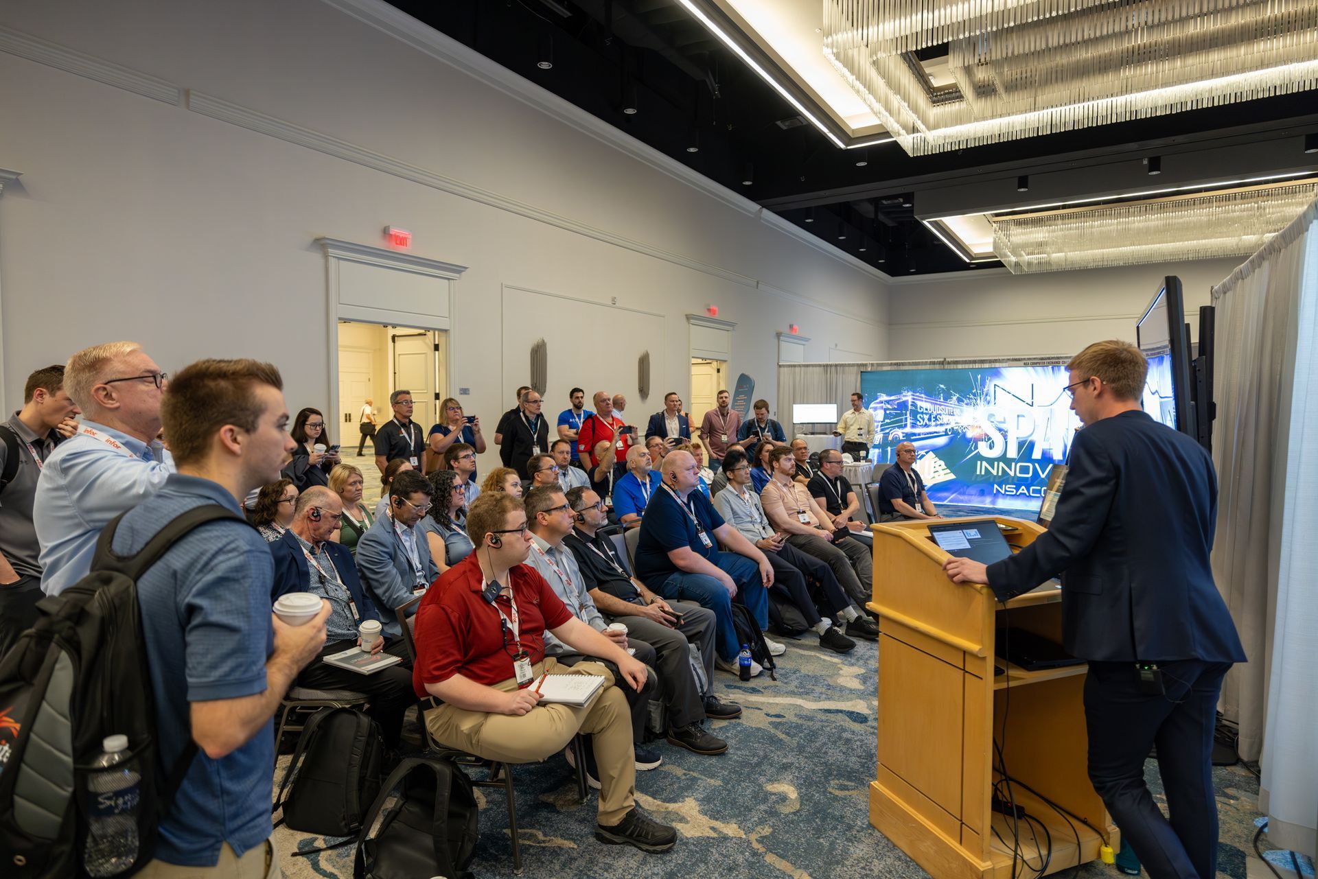 A man giving a presentation in a conference room to a large audience.