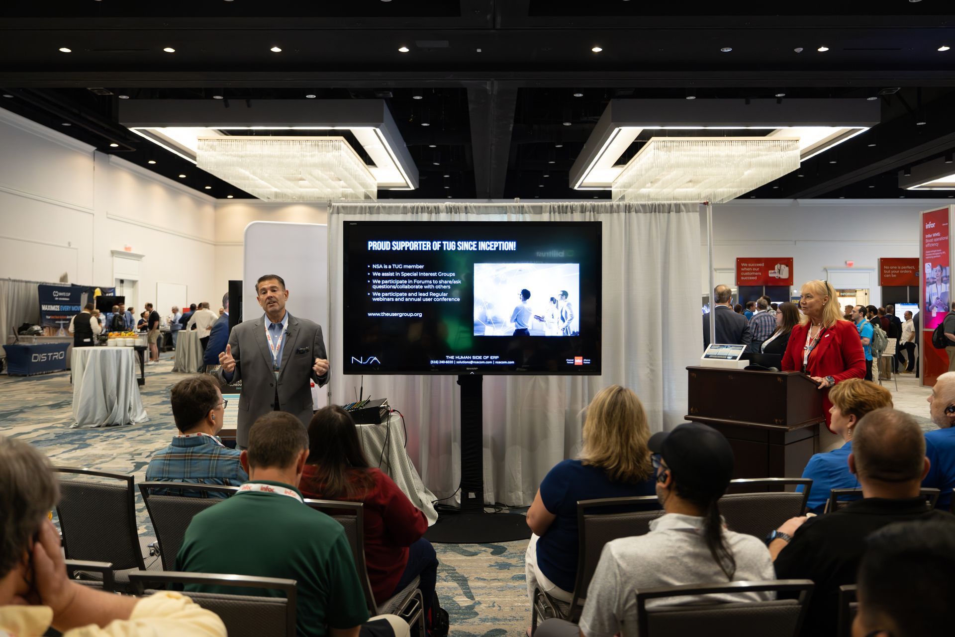 A man presents a slideshow at a conference, while a woman stands at a podium. Audience watches.