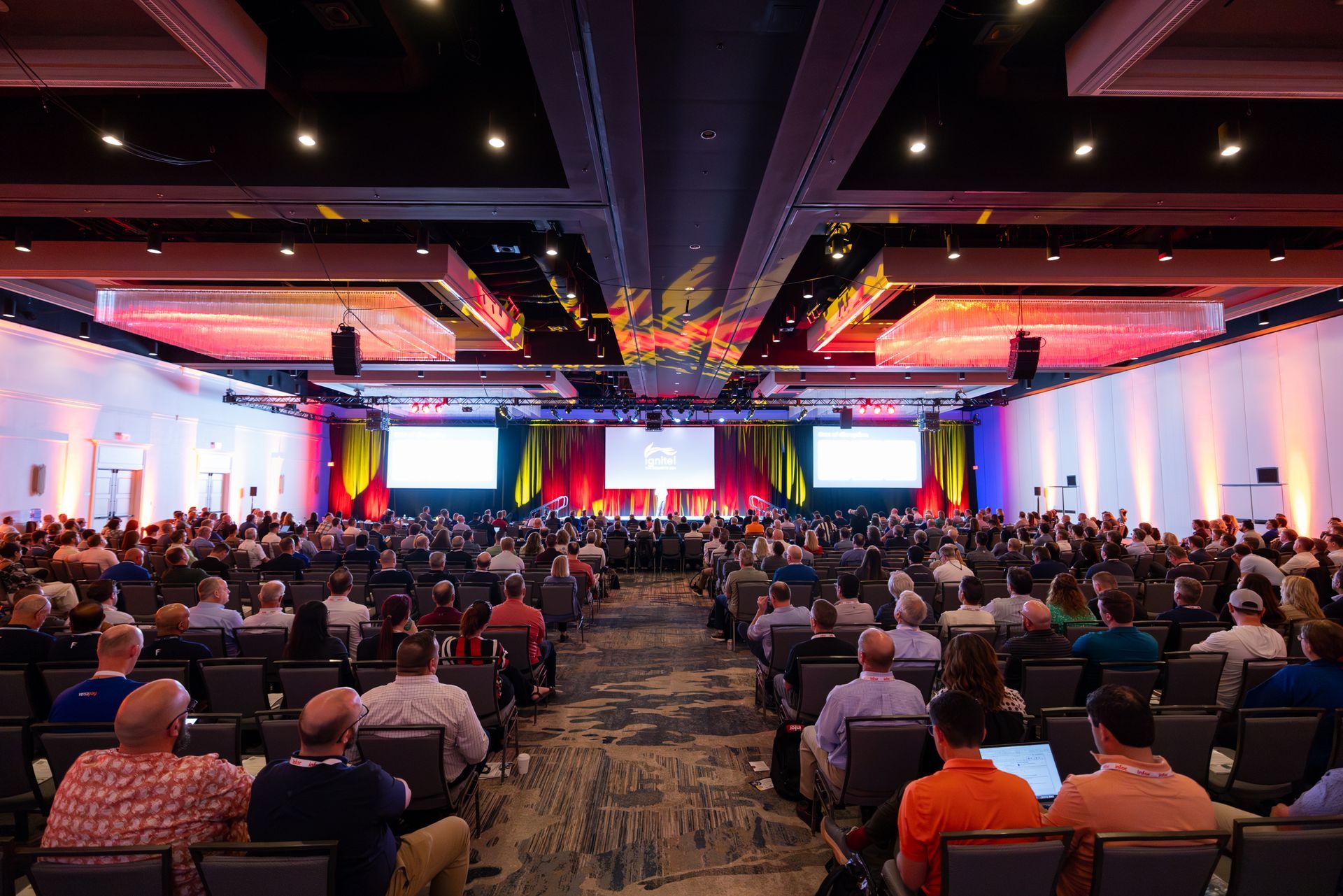 Large conference hall with audience seated; stage and screens at front.