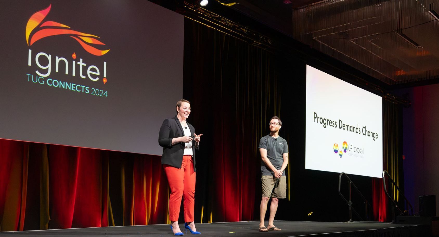 Two people on stage at a conference, Ignite!, speaking in front of large screens.