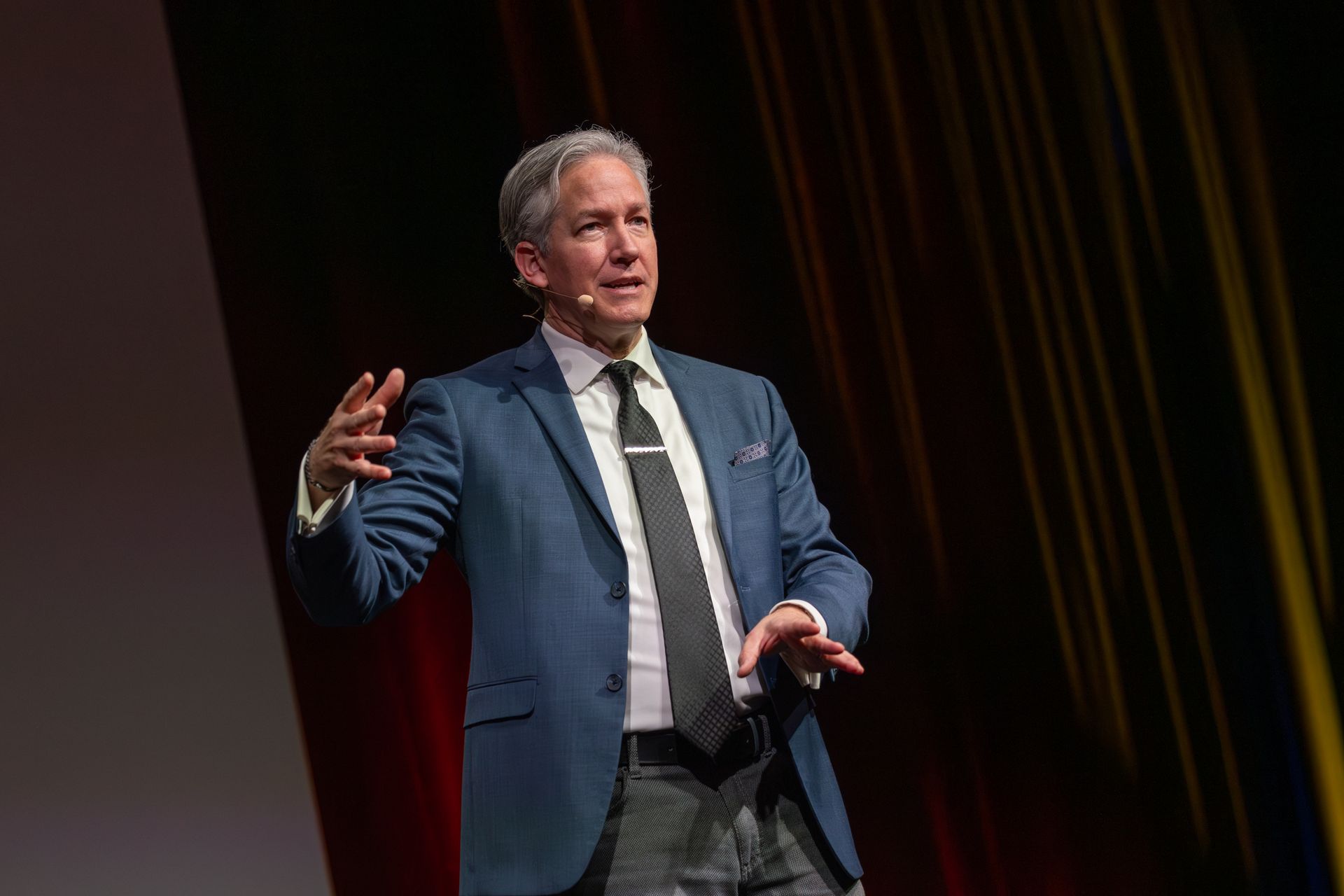 Man in blue suit gestures while speaking on stage.