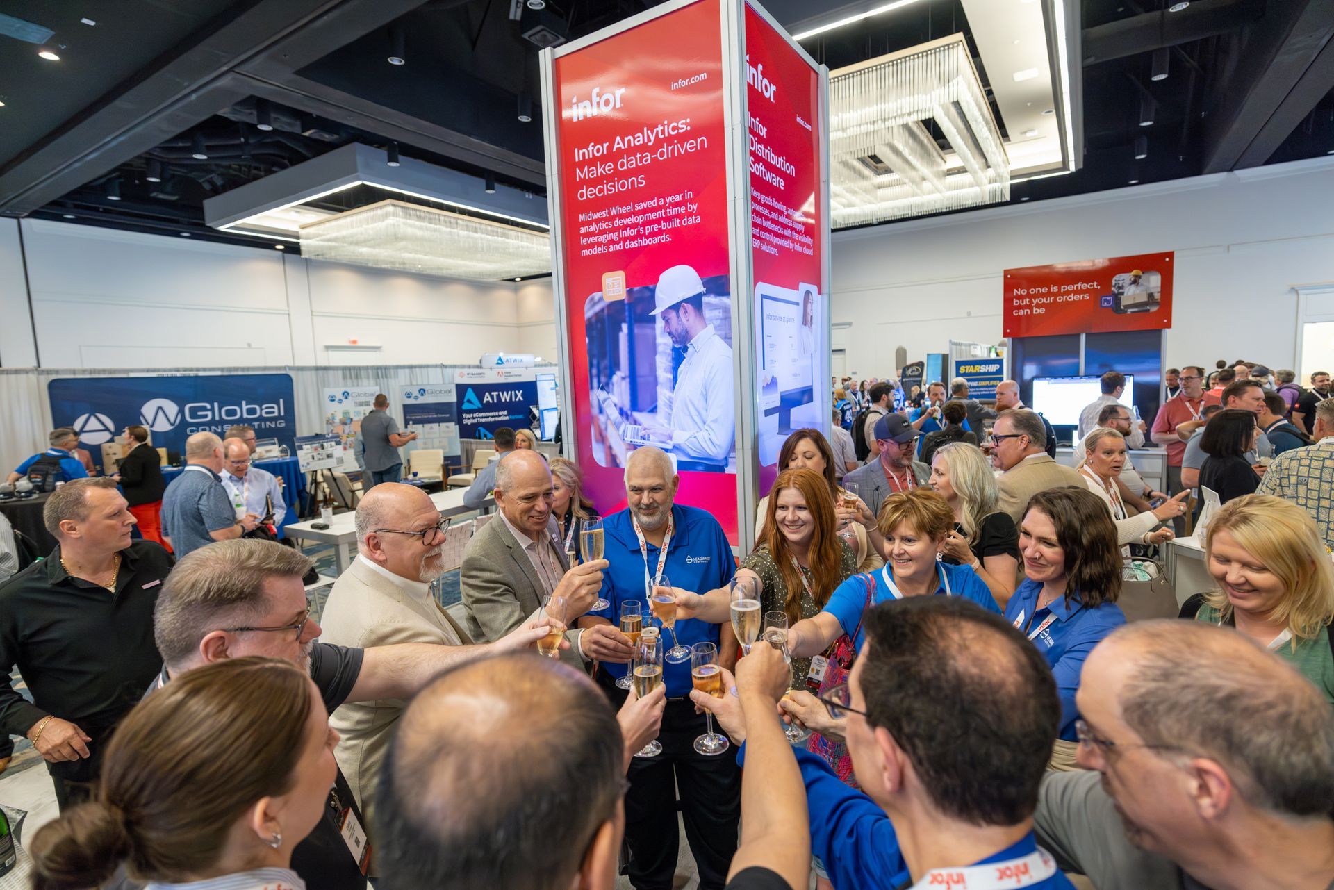 People toasting at an event, likely a trade show. A red pillar with signage is in the background.