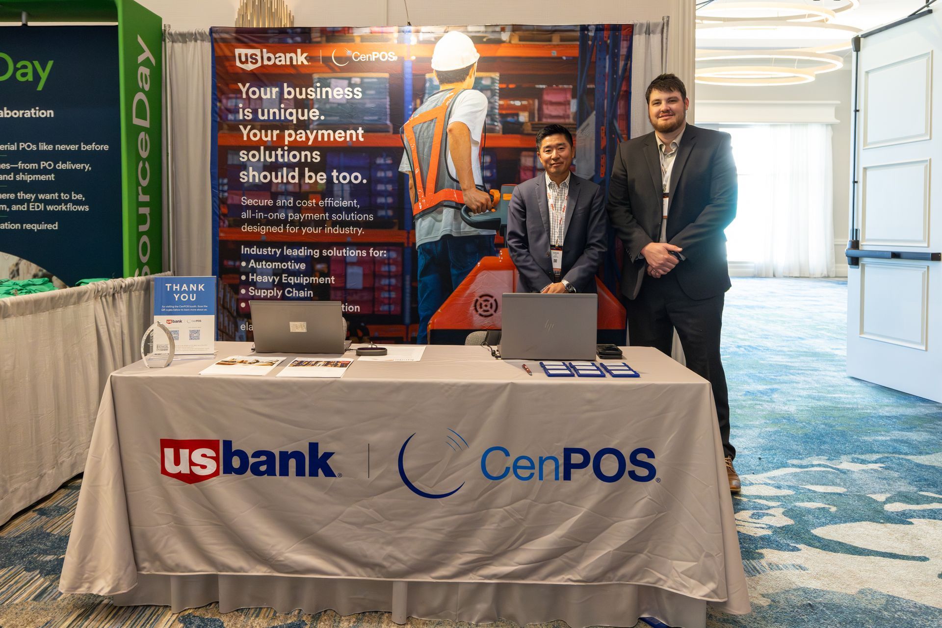 Two men at a US Bank and CenPOS booth. One man is seated; the other is standing. Both are wearing lanyards.
