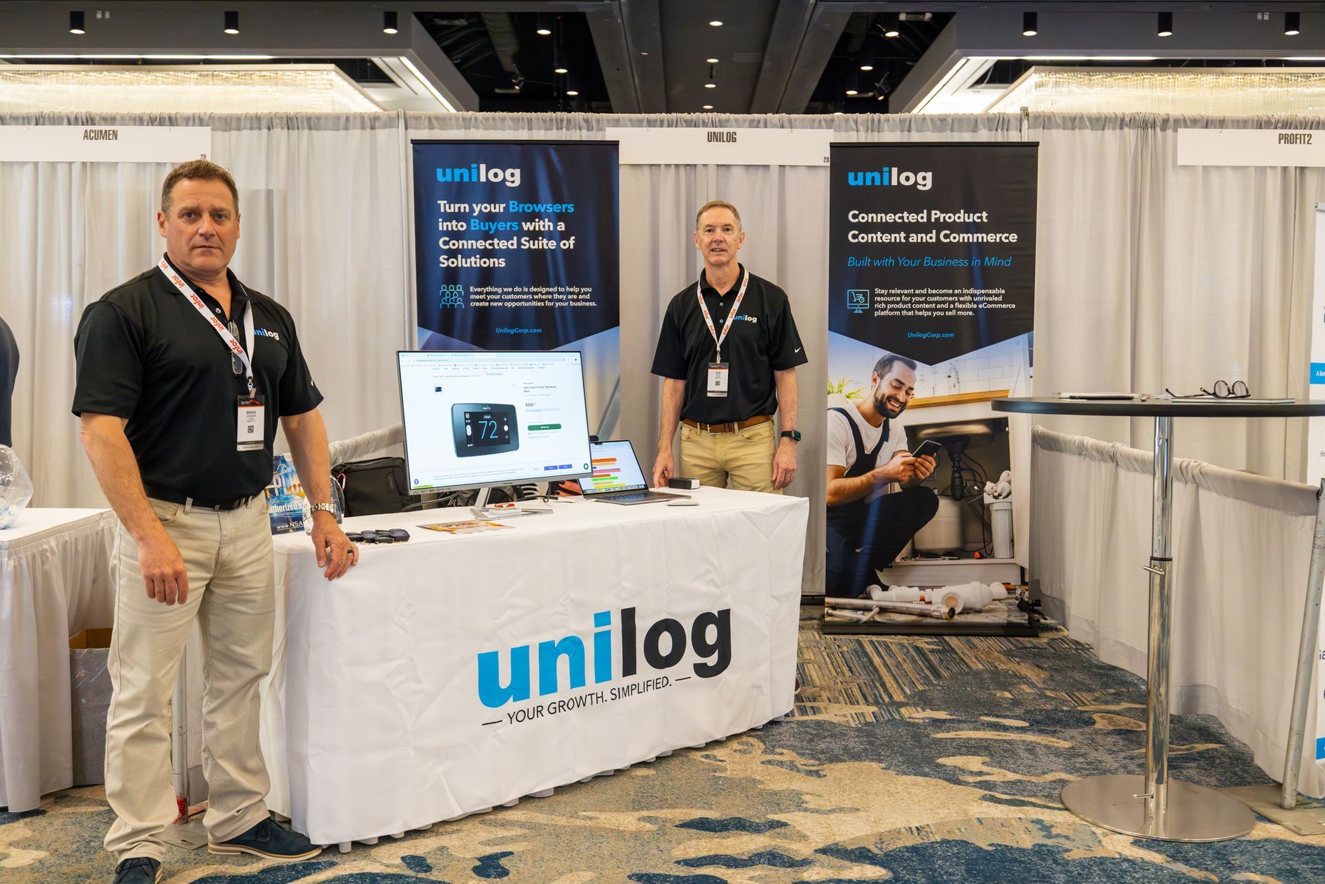 Two men stand at a trade show booth with 