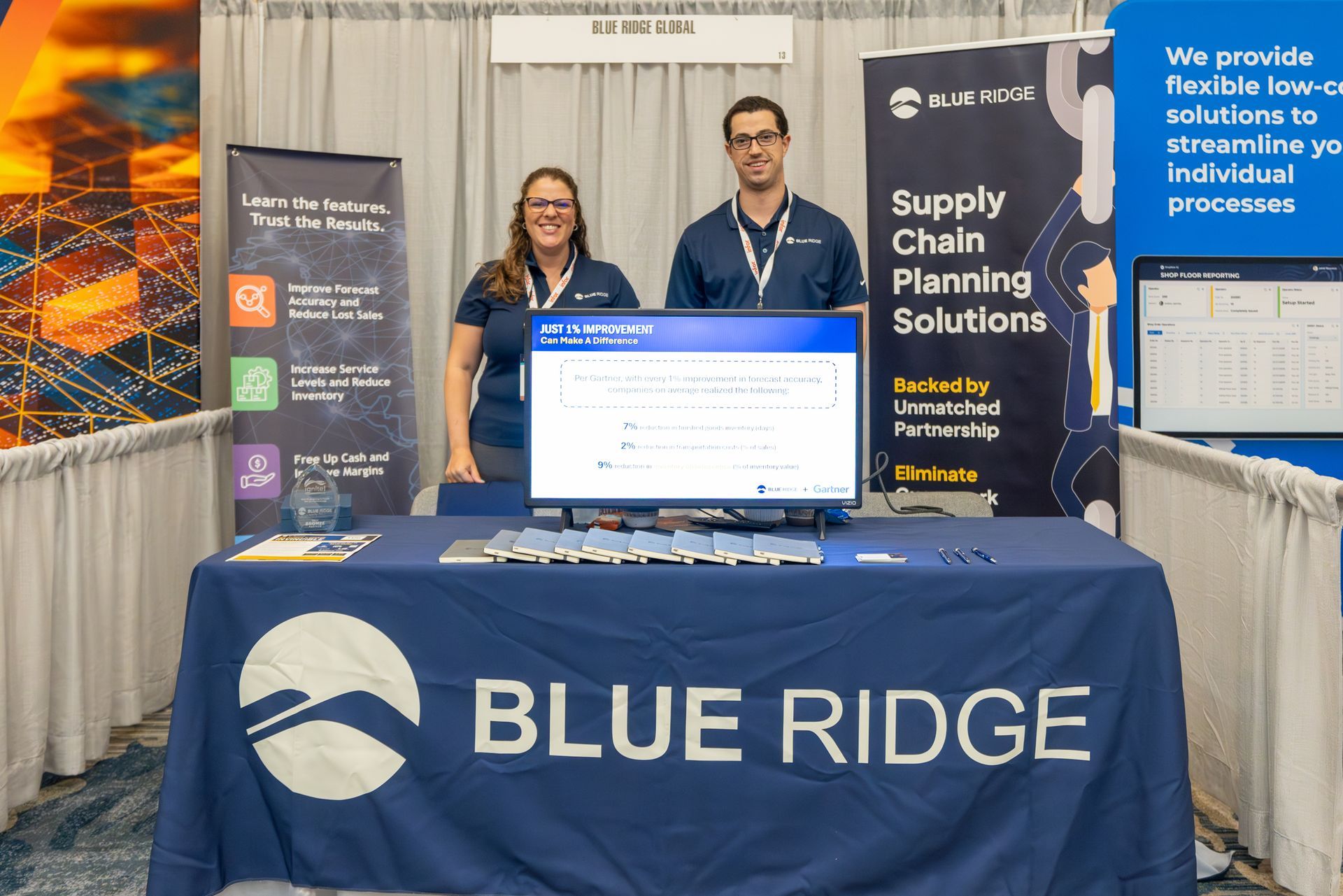 Two people at a Blue Ridge booth with a computer and banner for supply chain planning solutions.