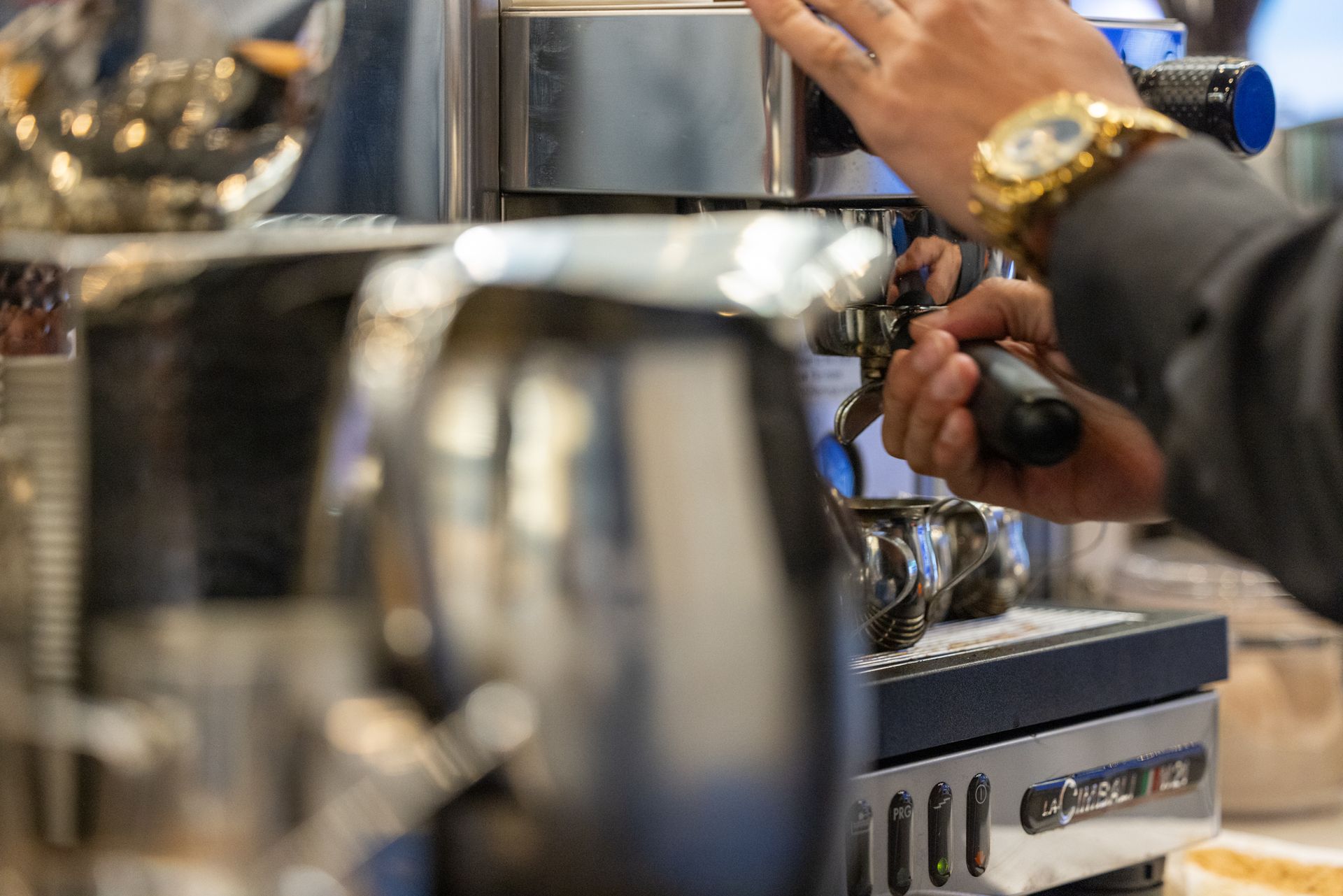 A person using an espresso machine, making coffee. Focus on hand, machine, and chrome pitcher.